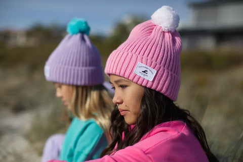 Two children at the beach with beanies on 