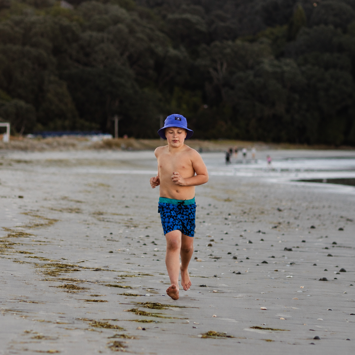 Boy wearing a blue bucket hat and blue hibiscus boardshorts at the beach