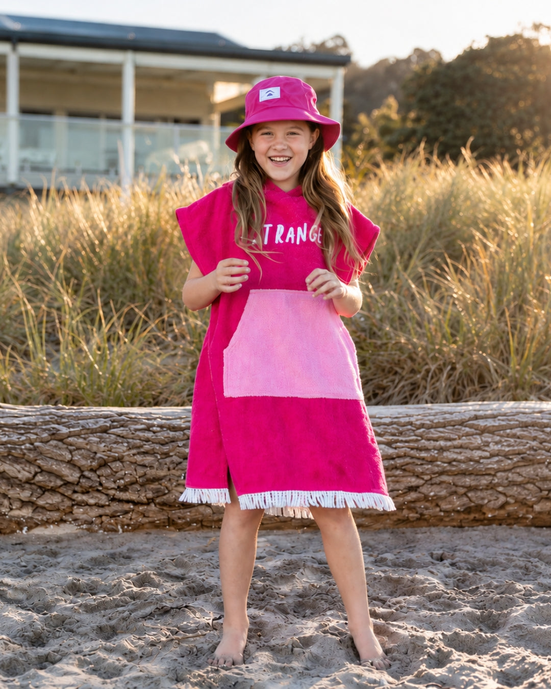 Girl wearing the fuchsia and pink Hello Stranger poncho towel at the beach